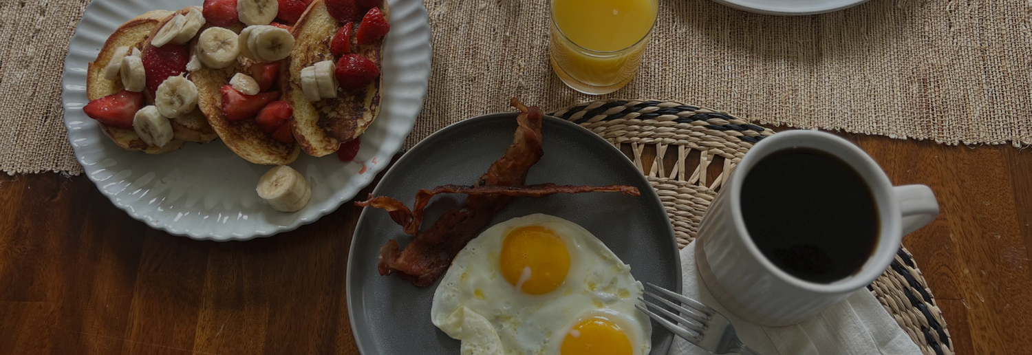 Breakfast scene with toast, eggs, bacon, and coffee on a wooden table.