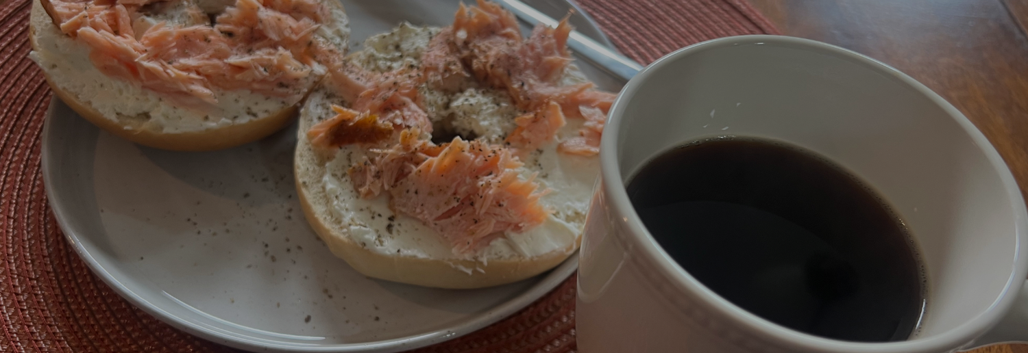 Two bagels with salmon on a plate next to a cup of coffee.