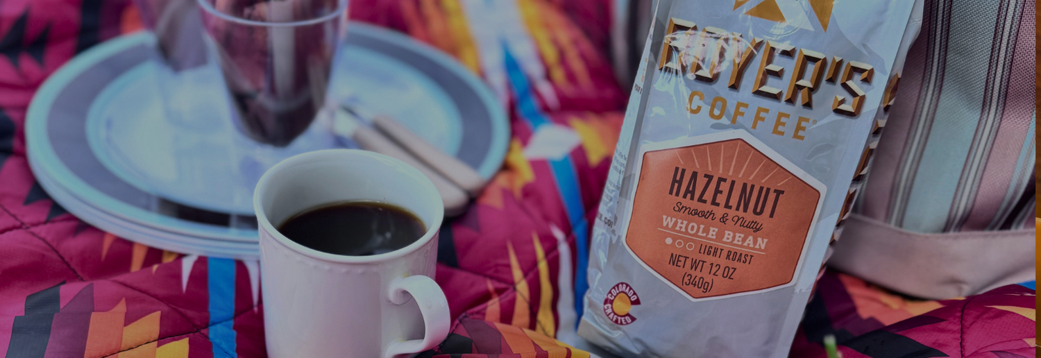Bag of Boyer's Coffee Hazelnut on a colorful tablecloth with a cup of coffee and a glass.