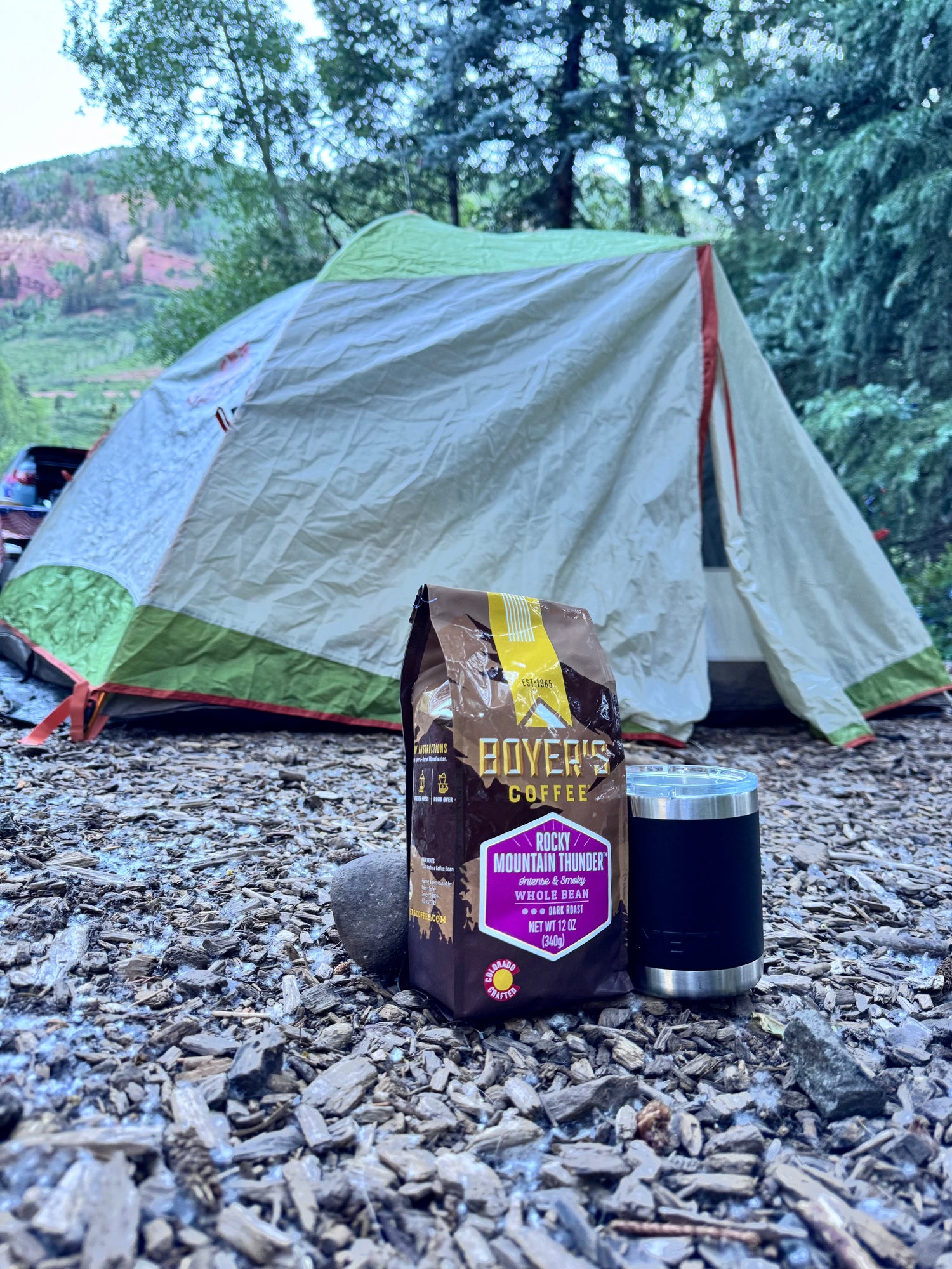 Boyer's Coffee bag and black tumbler in front of a tent in a camping setting