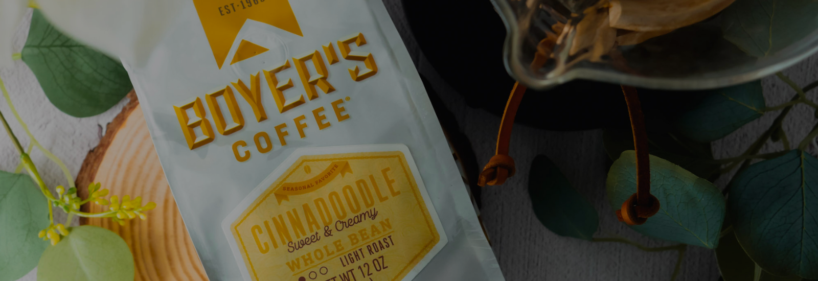 bag of cinnadoodle coffee next to a chemex and some yellow flowers and greenery