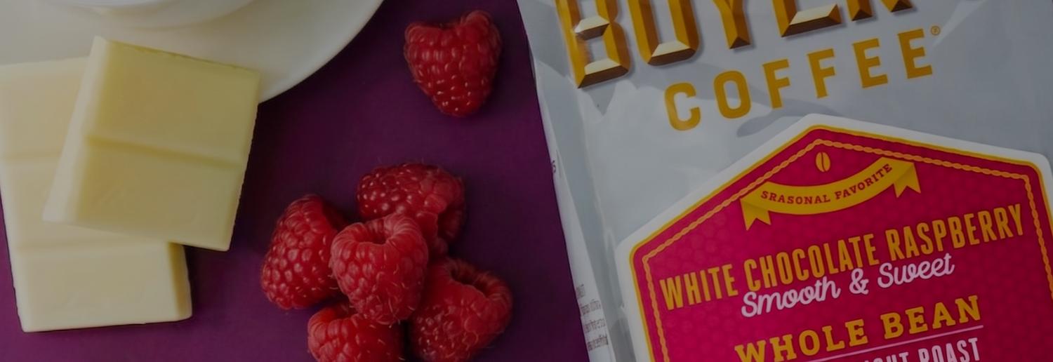 Bag of white chocolate raspberry coffee on a purple background with raspberries and white chocolate