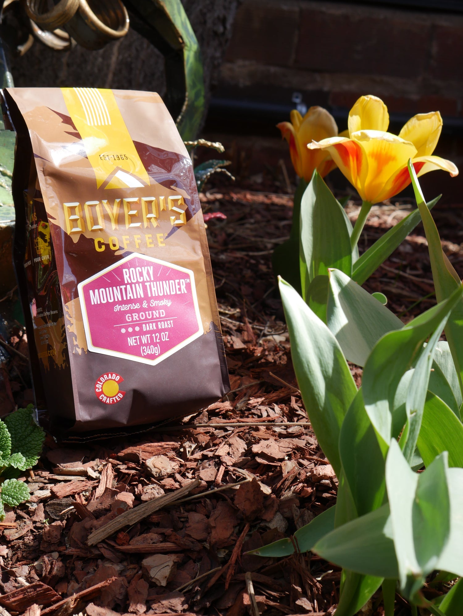 Packaged coffee on a wooden surface with flowers and leaves in the foreground